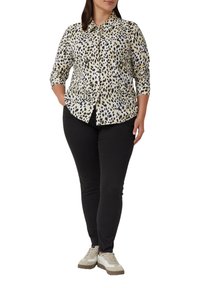 Lichtbeige overhemd met zwarte en bruine luipaardprint, lange mouwen, gecombineerd met zwarte broek en beige sneakers.