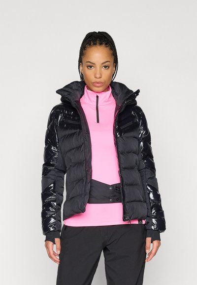 Μαύρο πούφφα τζάκετ με γυαλιστερά πάνελ, με κουκούλα που κλείνει με φερμουάρ και ελαστικούς μανσέτες, φορεμένο πάνω από ένα εφαρμοστό ροζ τοπ. Οι μαύροι παντελόνες ολοκληρώνουν το σύνολο.
