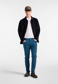 Črna jakna, bela majica in modrihlače. Obleka vključuje karirasto kapo in rjave čevlje ter prikazuje različne teksture in barve.