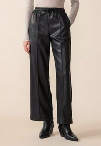 Black faux leather wide-leg pants with an elastic waistband and drawstring. Smooth texture, side pockets, and sleek tailoring detail.