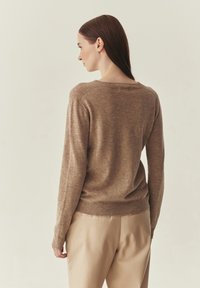 Pull en maille marron avec un col rond et un ourlet côtelé, associé à un pantalon beige clair. Le tissu semble doux avec une texture subtile.