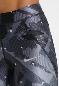 Leginsy w kolorze czarnym i szarym z wysokim stanem, w wzór, z małym białym logo Nike w kształcie „swoosh” na biodrze.