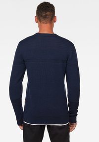 Marineblauer Strickpullover mit strukturierten Mustern und gerippten Bündchen. Verfügt über einen Rundhalsausschnitt und einen geraden Saum. Der Stoff wirkt weich und von mittlerem Gewicht.
