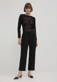 Top in mesh a maniche lunghe a strisce zebra neri e beige abbinato a pantaloni neri a vita alta, con cintura nera e scarpe a punta.