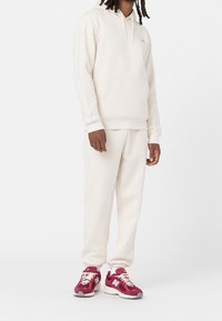 Krémová mikina s kapucí a přední kapsou, s žebrovanými manžetami, doplněná o sladěné tepláky. Bordó sportovní boty s bílými detaily a logem.