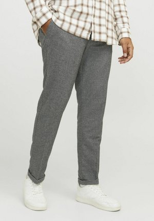 Pantalons gris fuselés en tissu texturé, avec poches latérales, associés à des baskets blanches et une chemise à carreaux.