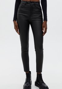 Schwarze dünne Hosen aus Kunstleder mit hoher Taille, Fronttaschen und Gürtelschlaufen. Sie verfügen über eine glatte Textur und ein figurschmeichelndes Design.