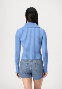 Pull en rib avec un col montant de couleur bleu clair, présentant des manches longues et une taille ajustée, associé à un short en denim taille haute.