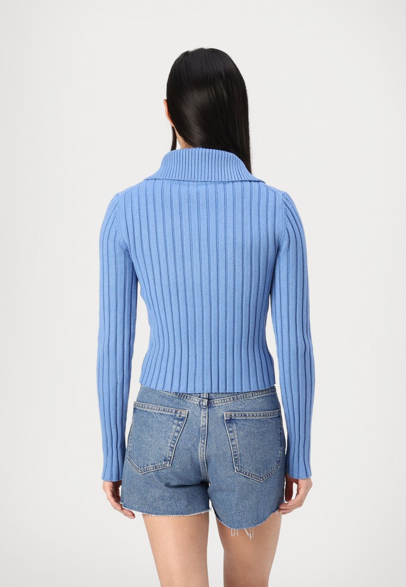 Lichtblauwe geribbelde trui met een hoge kraag, voorzien van lange mouwen en een getailleerde taille, gecombineerd met hoge spijkerbroekshorts.