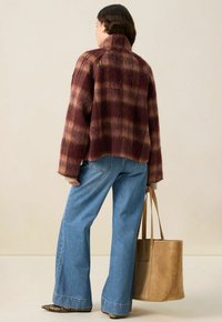 Veste en plaid moelleux mauve et beige, coupe décontractée avec un col haut, associée à un jean large bleu clair et un sac fourre-tout en daim beige.