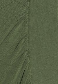 Olivgrön stickad tyg med en texturerad del som har smala vertikala veck på ena sidan och en slät, utan veck, yta på den andra.