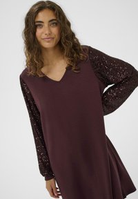 Abito borgogna con scollatura a V e maniche lunghe in paillettes nere lucide. Il tessuto è morbido, con una silhouette svasata.