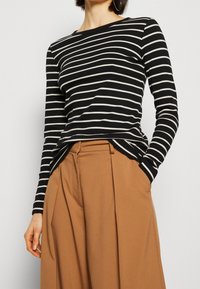 Camicia a maniche lunghe a righe bianche e nere realizzata in un tessuto morbido, con scollatura rotonda e un taglio rilassato, abbinata a pantaloni larghi marroni.