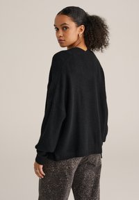 Maglione nero lavorato a maglia con vestibilità ampia, spalle scese e polsini a coste, abbinato a pantaloni marroni con stampa leopardata testurizzata.