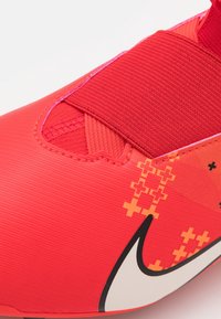 Rød fodboldstøvle med tekstureret syntetisk overdel, elastisk strop og karakteristisk orange mønster. Sort og hvidt logo er tydeligt vist.