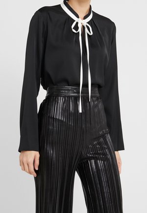 Black long-sleeve blouse with white tie at neckline paired with high-waist, shiny black pleated pants.