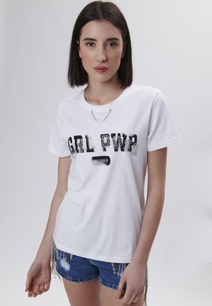 Weißes Baumwoll-T-Shirt mit schwarzem und silbernem Glitzertext "GRL PWR INFLUENCER." Getragen mit blauen Denim-Shorts, die über silberne Fransen verfügen.
