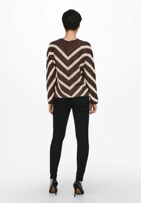Pull beige et marron à motif chevron avec un col rond, associé à un jean skinny noir et des talons hauts noirs.