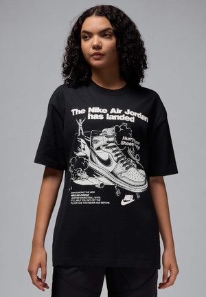 T-shirt nera in cotone con stampa grafica di una scarpa Nike Air Jordan e testo. Maniche corte, vestibilità ampia, con illustrazioni e testo bianchi.