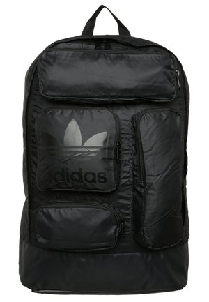 Musta Adidas-reppu, jossa on useita etutaskuja vetoketjuilla, mukaan lukien yksi Adidas-trefoil-logolla.