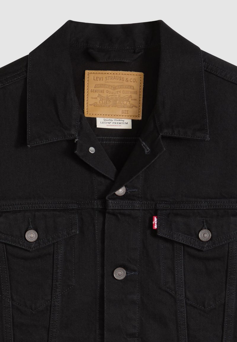 Black denim jacket with a pointed collar, chest pockets, silver hardware, and a leather label featuring brand details sewn into the neckline.