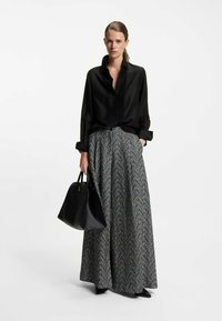 Camicia nera con bottoni e maniche lunghe, abbinata a una lunga gonna a motivo herringbone in bianco e nero. Accessorio: borsa nera.