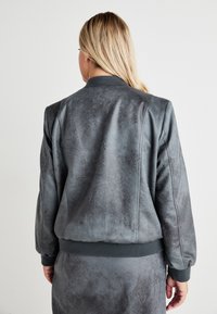 Grå bomberjakke med teksturfinish, ribbestrikkede mansjetter og hem. Har en jevn, svakt glansfull overflate med en avslappet passform.