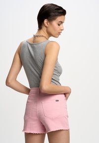 Pelēka bezmugurkaula topa ar apaļu izgriezumu, apvienota ar rozā džinsu šortu ar saplaisājušiem maliņām un redzamām aizmugurējām kabatām. Ķēdes detaļa ap kakla izgriezumu.