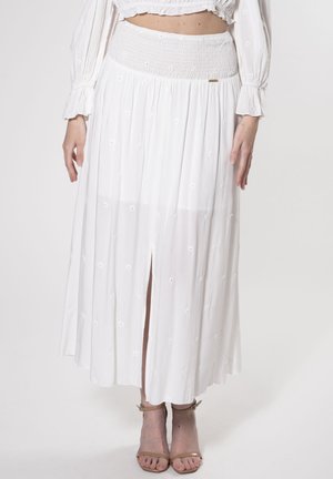 Falda midi blanca y fluida con cintura fruncida, que presenta pequeños detalles florales bordados y una abertura frontal. Tejido ligero, textura suave.