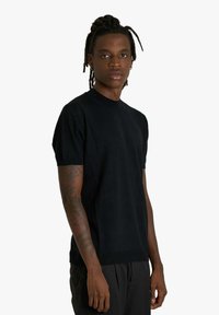 T-shirt nera a maniche corte in maglia con scollo rotondo e orlo a coste. Texture liscia, design aderente e dettagli di cucitura sottili.