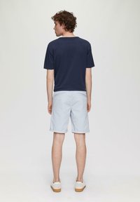 Marineblaues Kurzarm-T-Shirt kombiniert mit hellblauen Shorts. Die Shorts haben einen umgeschlagenen Saum und zwei Gesäßtaschen und werden mit hellen Schuhen getragen.