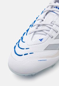 Scarpa da calcio bianca con accenti blu, materiale sintetico testurizzato e motivi in gomma distintivi. Presenta lacci e logo stampato.