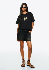 Black oversized t-shirt with gold star graphic, paired with a black denim mini skirt and black strappy sandals. Smooth fabric and design.