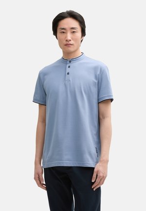 Polo shirt azzurro chiaro a maniche corte con colletto alto, patta con tre bottoni e bordi navy sulle maniche; presenta un logo discreto orlato sul fondo.