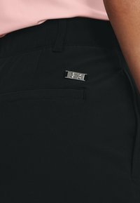 Black athletic pants made of smooth fabric, featuring a small silver logo accent and a side pocket with a flat design.