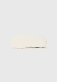 Sole of a sneaker, made of rubber, in cream color. Features textured grip patterns and rounded shape with a slightly raised heel.