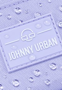 Lila tyg med vattendroppar har en texturerad yta. En framträdande gummilabel står det "JOHNNY URBAN" med en glasögonikon.