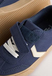 Baskets en daim bleu marine avec accents beige et semelle en caoutchouc texturée ; dotées d'une fermeture à lacets et à velcro, logo dessiné en beige.