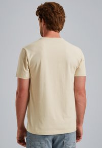 Camiseta de manga corta en algodón beige claro, con cuello redondo y corte sencillo. Textura suave sin patrones ni acentos visibles.