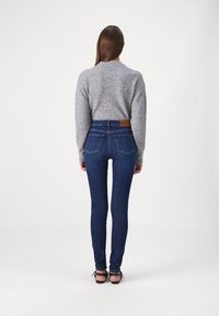 Suéter gris combinado con unos jeans skinny azul oscuro de tiro alto, con bolsillos traseros y una etiqueta de cuero en la cinturilla. Tacones negros completan el look.
