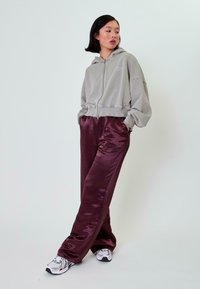 Grijze cropped zip-up hoodie met geribde zoom, gecombineerd met glanzende bordeaux brede broek en witte sneakers met zwarte accenten.
