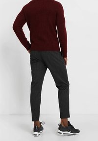 Maglione a maglia color bordeaux, pantaloni slim-fit neri con texture e scarpe sportive nere con accenti bianchi. Focalizzati su colore, texture e design.