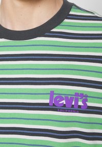 T-shirt rayé vert, noir, blanc et bleu avec un col noir et un logo violet "Levi's California" sur la poitrine.