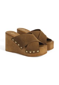 Sandales compensées en suède marron avec un design à bande croisée, bout ouvert et clous dorés sur le côté. Présente une plate-forme en bois.