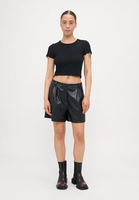 Fekete bordázott cropped top, fodros szegéllyel, magas derekú fekete bőr sorttal és fekete fényes bokacsizmával párosítva.