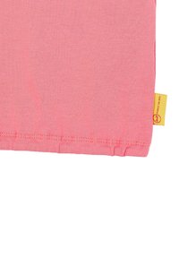 Růžové bavlněné tričko s kulatým lemem, které má žlutou tag na boku. Hladká textura, jednoduchý design a žádné viditelné vzory.