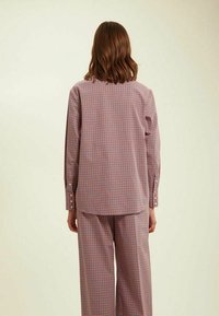 Ensemble deux pièces à motif à carreaux comprenant une chemise ample et un pantalon large, tous deux dans des tons de rose et de bleu. Détails de boutons sur les manches.