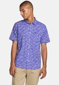Short-sleeve button-up shirt in vibrant purple with a white rose pattern. Made of lightweight fabric with a collar and front pocket detail.
