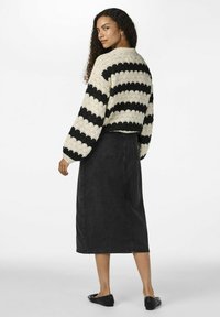 Gestrickter, kurzer Pullover mit Schwarz- und Cremestreifen, kombiniert mit einem schwarzen Jeans-Maxikleid und flachen schwarzen Schuhen, von hinten betrachtet.