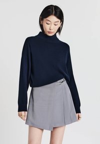 Maglione a collo alto blu navy abbinato a una gonna a portafoglio grigia chiara con fibbia laterale, tessuto morbido e design plissettato.